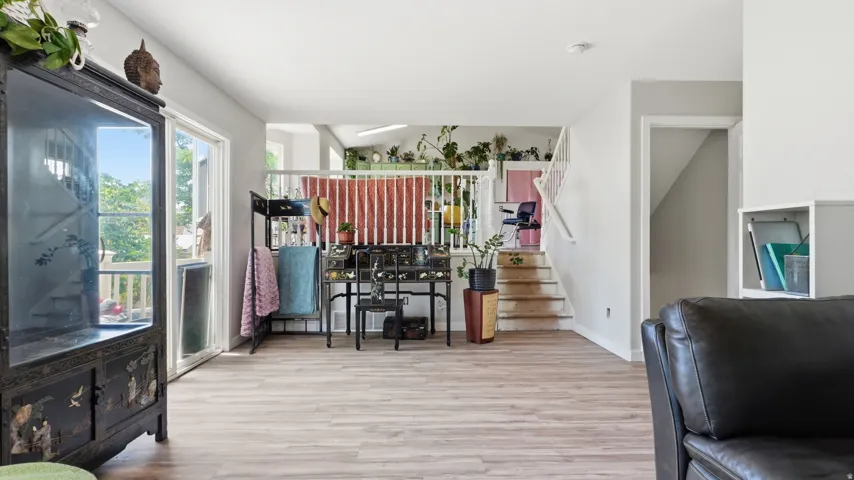 Spacious open-concept interior featuring light wood-finish flooring, a white-painted stairwell, and a built-in wall shelf