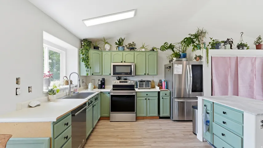 Kitchen featuring green cabinetry, stainless steel appliances, and wood-finish flooring