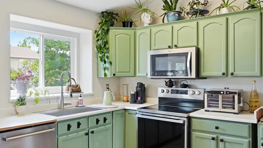 Kitchen featuring light green cabinetry with black hardware, white countertops, and stainless steel appliances