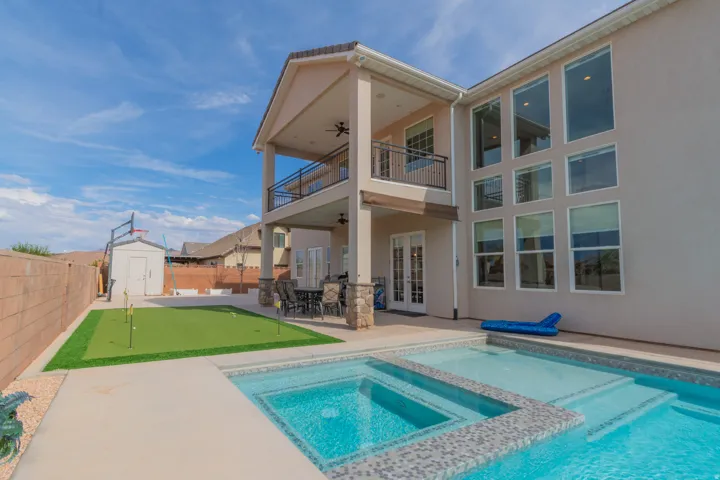 Backyard oasis featuring a swimming pool with integrated spa, a putting green, and an expansive covered patio