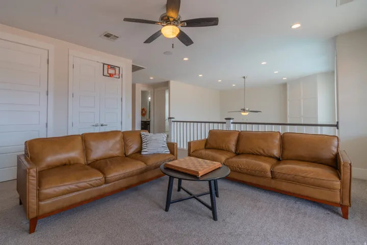 Carpeted loft space featuring a ceiling fan with integrated lighting, recessed lighting, white paneled doors, and a white balustrade with a dark handrail