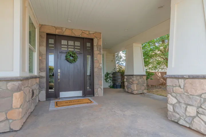 Covered entry featuring a dark wood door with glass paneling, stone facade accents, and a concrete patio