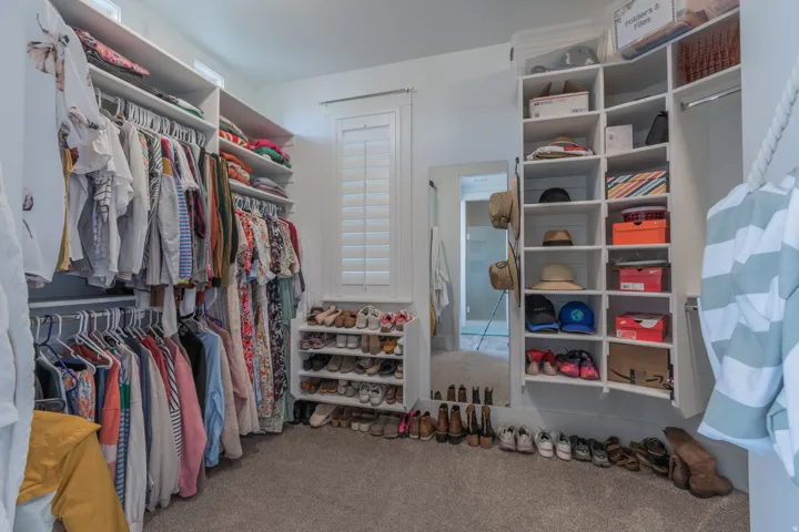 Expansive walk-in closet featuring extensive built-in shelving, multiple hanging rods, shuttered window, soft carpet flooring, and a full-length mirror
