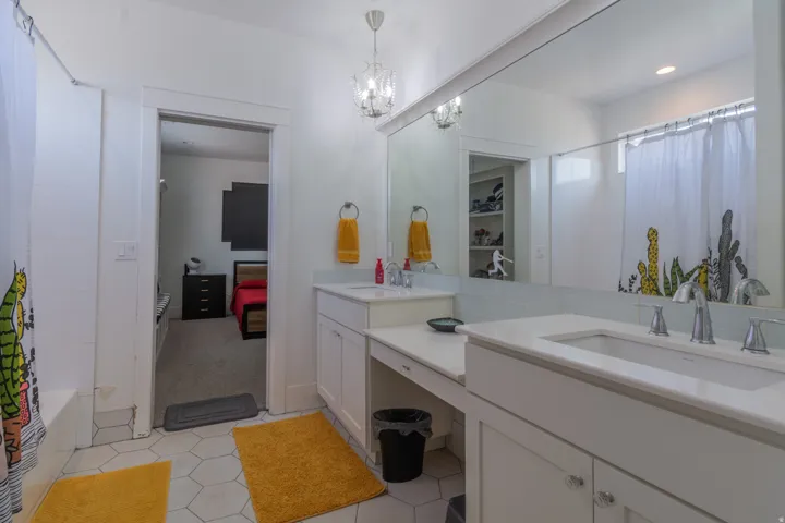 Bathroom featuring dual vanities with integrated sinks, white cabinetry, and a large wall-mounted mirror