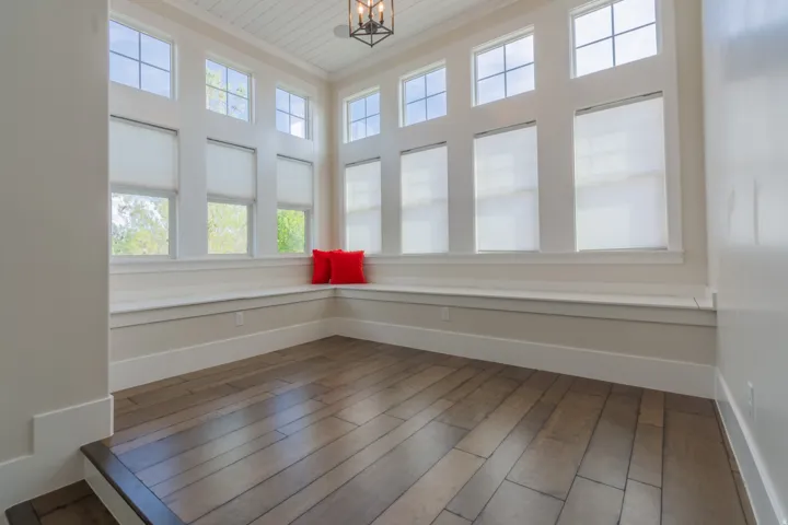 Sun-drenched room featuring extensive window-lined walls, a built-in window bench, wood-finish flooring, and a coffered ceiling with a black metal chandelier