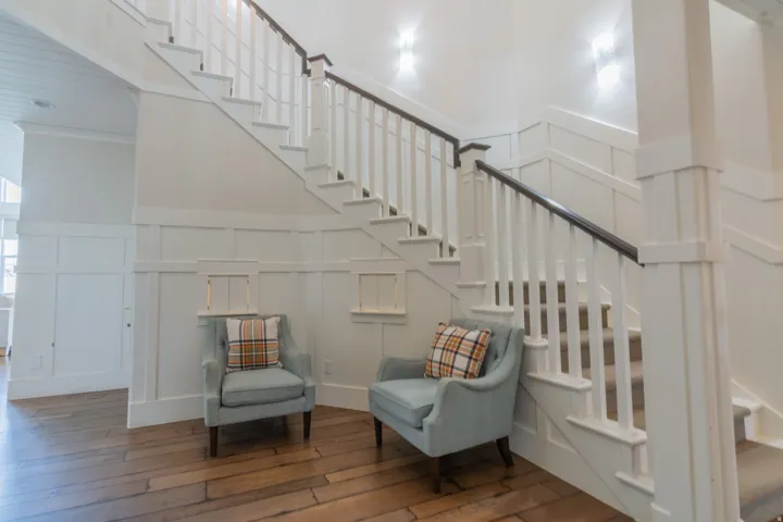 Hardwood flooring complementing the white paneled walls and staircase with dark wood handrails