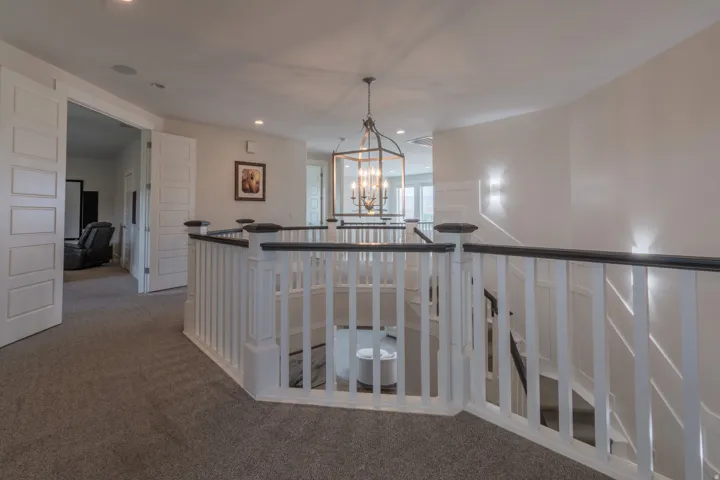 Upper-level landing featuring plush carpet flooring, a white and black staircase railing, recessed lighting, and a prominent chandelier with multiple bulbs