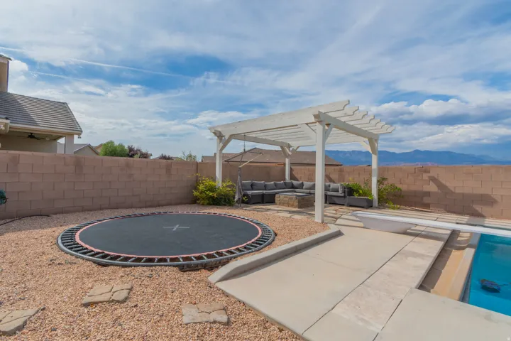 Backyard featuring a built-in swimming pool, a white pergola-covered patio area, and a large inground trampoline