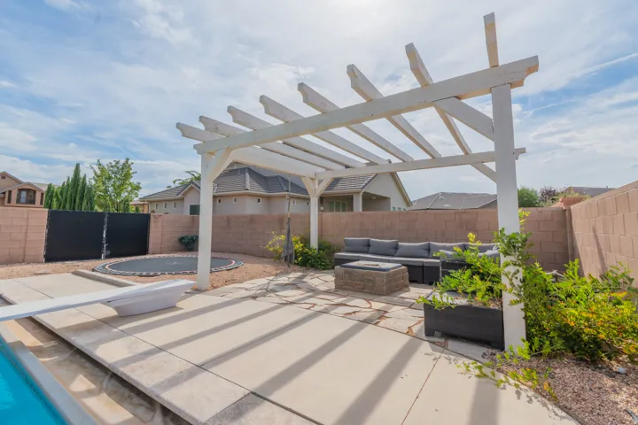 Outdoor living space featuring a white pergola, stone patio, and block privacy wall
