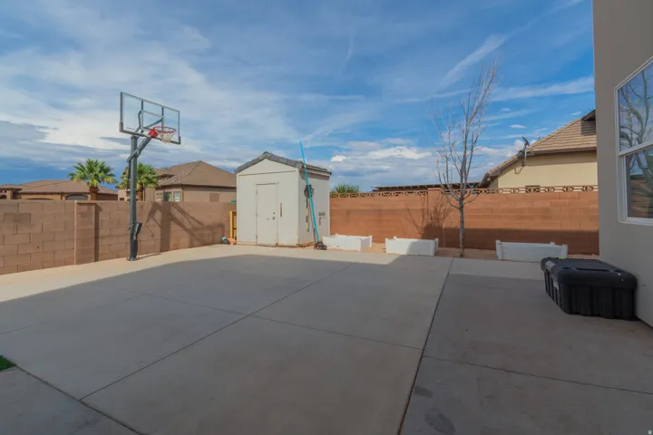 Expansive concrete patio area featuring a basketball hoop, a detached storage shed, a decorative block wall, and perimeter landscaping
