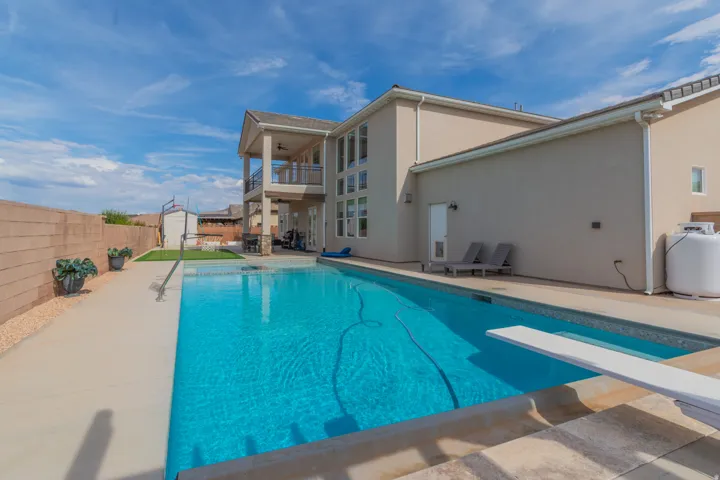 Backyard featuring a rectangular swimming pool with a diving board, surrounding concrete patio, and a two-story exterior with a covered balcony