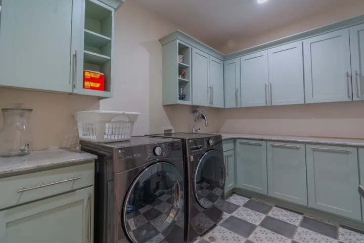 Laundry room featuring extensive built-in cabinetry with light blue shaker-style doors, speckled countertops, and a checkerboard floor tile pattern