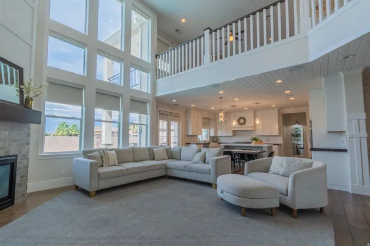 Two-story living area featuring a fireplace with stone tile surround, floor-to-ceiling windows with roller shades, and wood-finish flooring