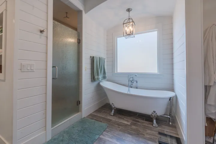Freestanding clawfoot tub with polished chrome fixtures, shiplap wall paneling, wood-finish flooring, and a glass-enclosed shower