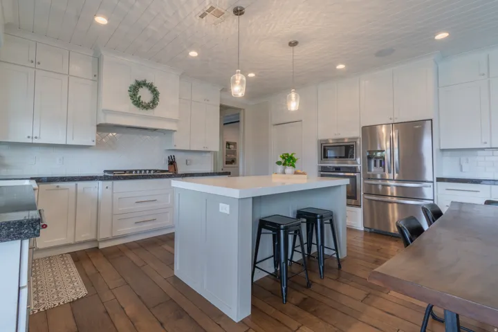 Spacious kitchen featuring an expansive center island with seating, stainless steel appliances, white cabinetry, dark stone countertops, and wood-finish flooring