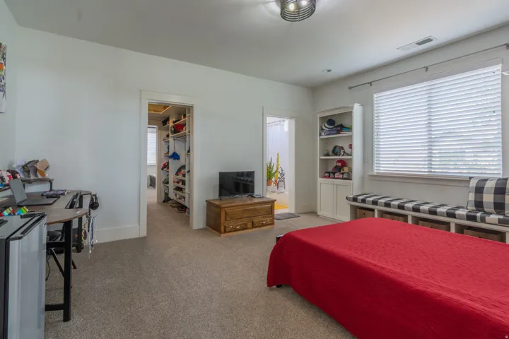 Carpeted room featuring a window with blinds, a built-in window bench with storage cubbies, a built-in bookcase with lower cabinetry, and two doorways leading to additional interior spaces