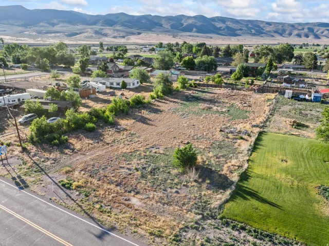 Expansive undeveloped land parcel featuring a paved road frontage, partially vegetated terrain, and distant mountain backdrops