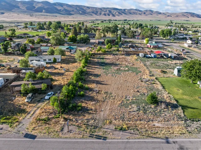 Expansive vacant land bordered by mature trees and a paved road, featuring a distant mountain backdrop