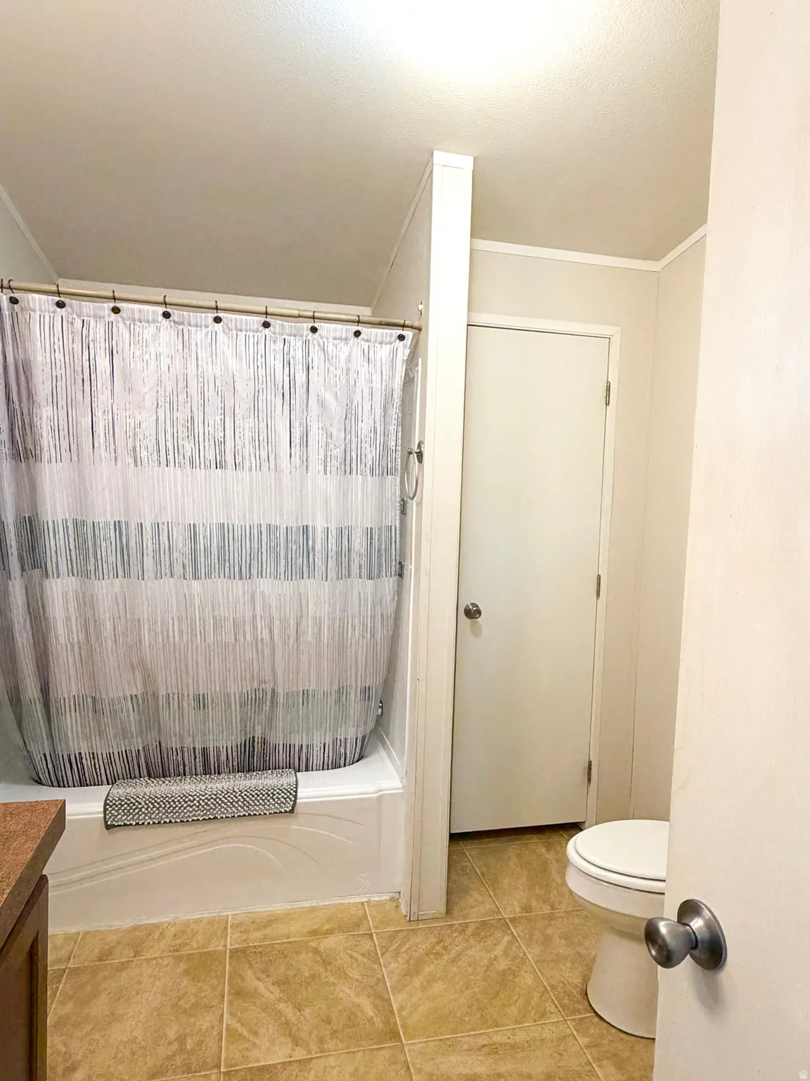 Bathroom featuring a white tub and shower enclosure, tan tile flooring, and a white toilet
