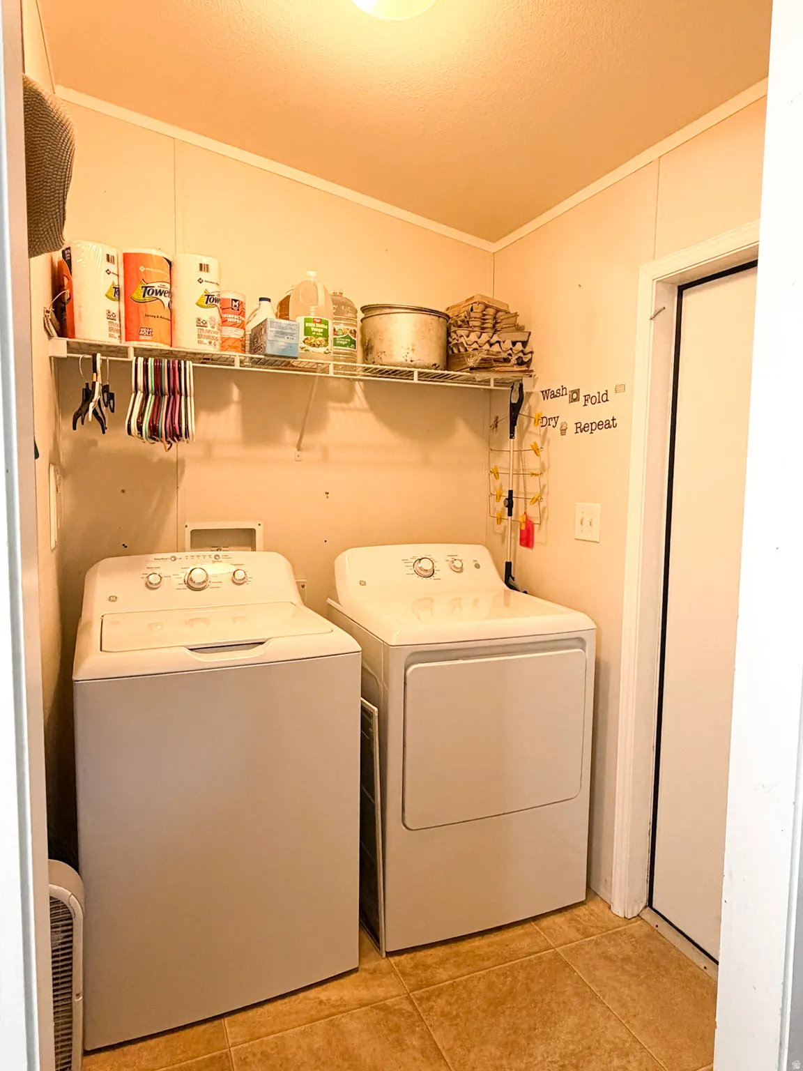 Laundry area featuring tile flooring, a built-in wire shelf, overhead lighting, and white paneled walls