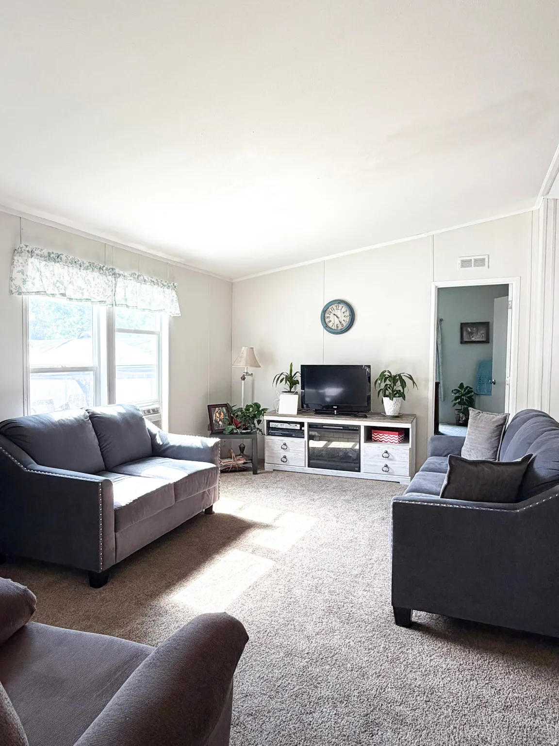 Spacious living area featuring neutral carpeting, white vertical paneled walls, and a recessed media console with an integrated electric fireplace