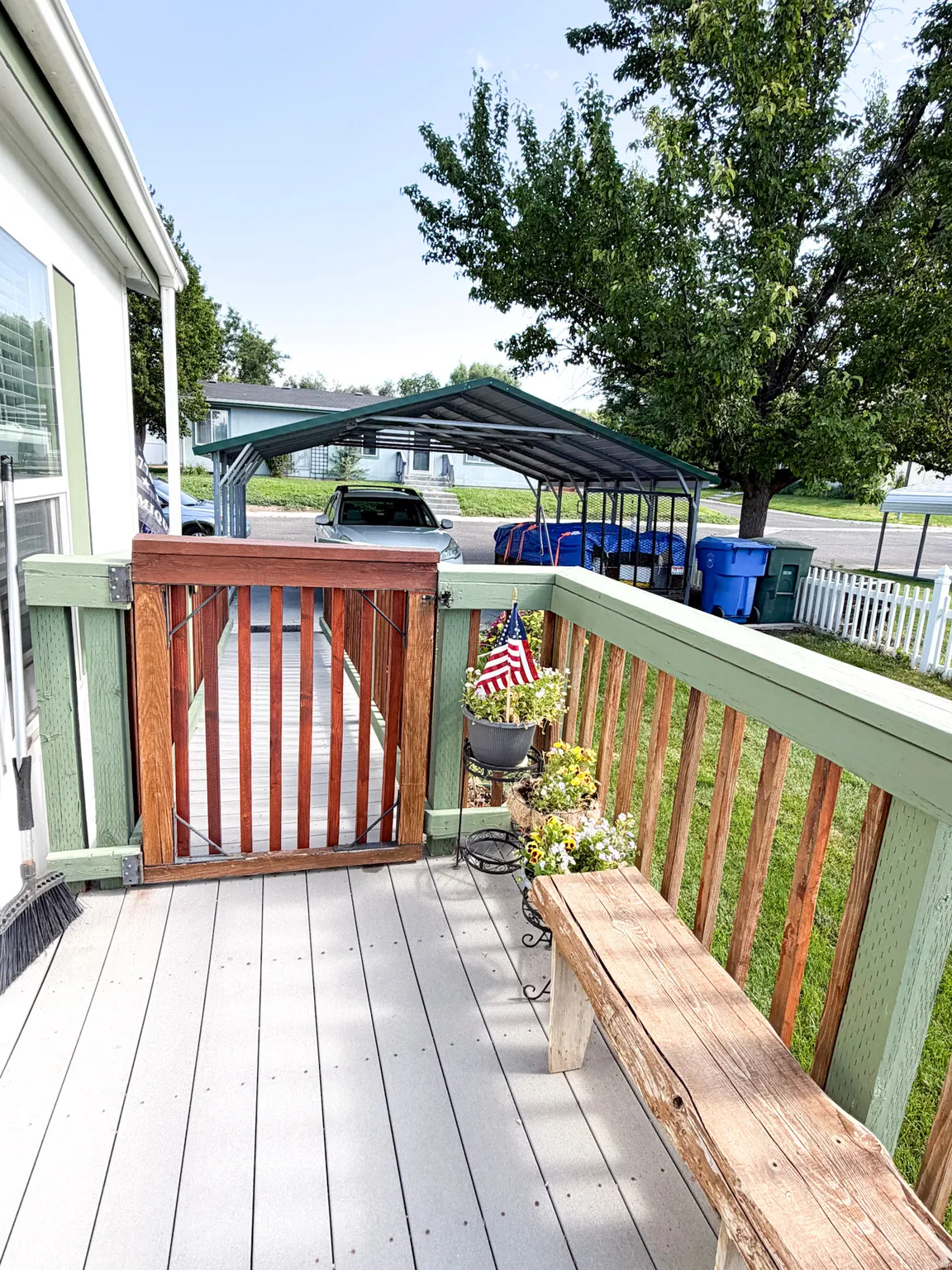 Spacious deck with composite decking and light green railings, featuring a wooden gate and a natural wood bench