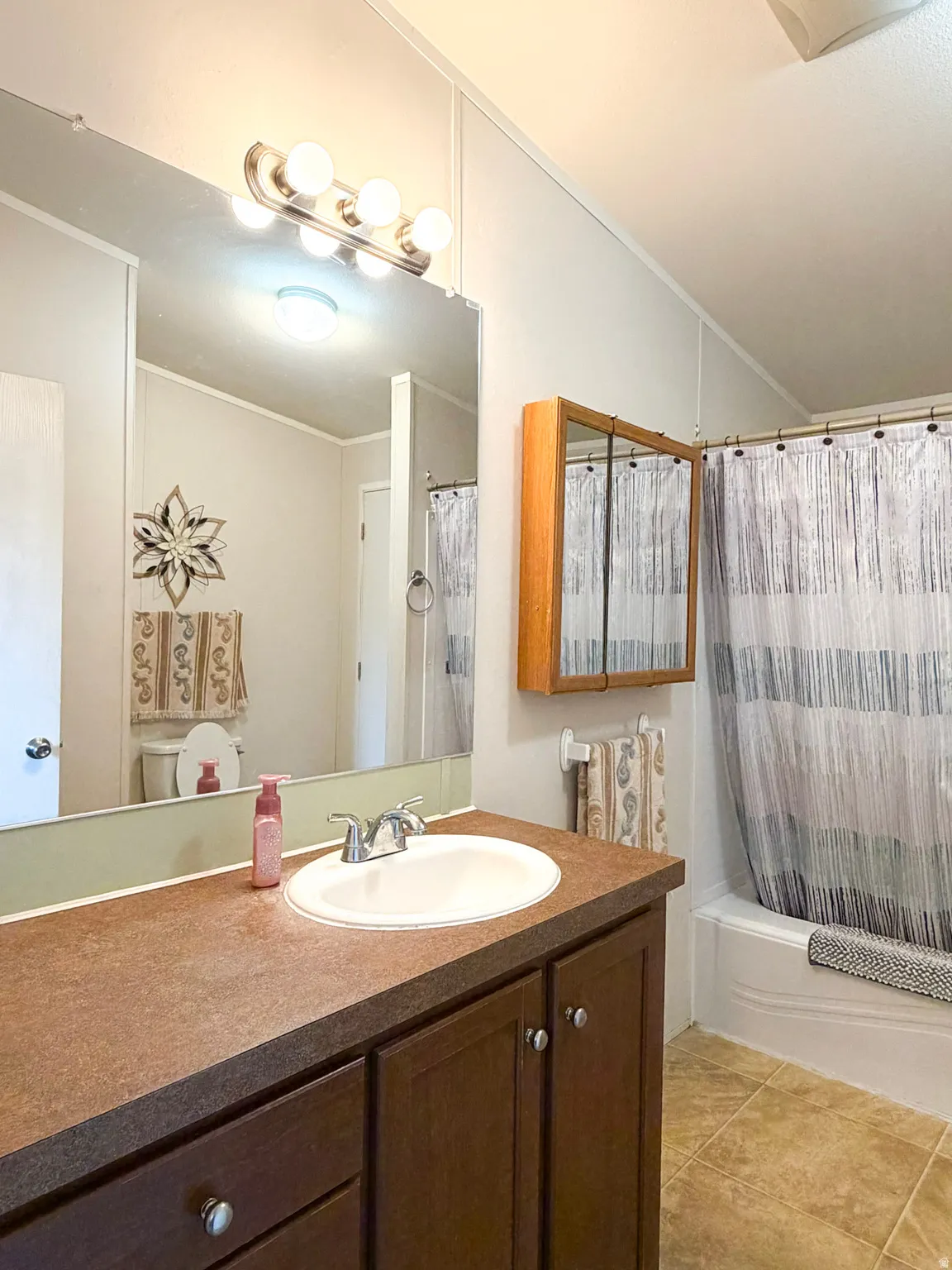 Bathroom featuring a dark wood-finish vanity with a built-in sink, a large wall mirror, and a full bathtub with shower