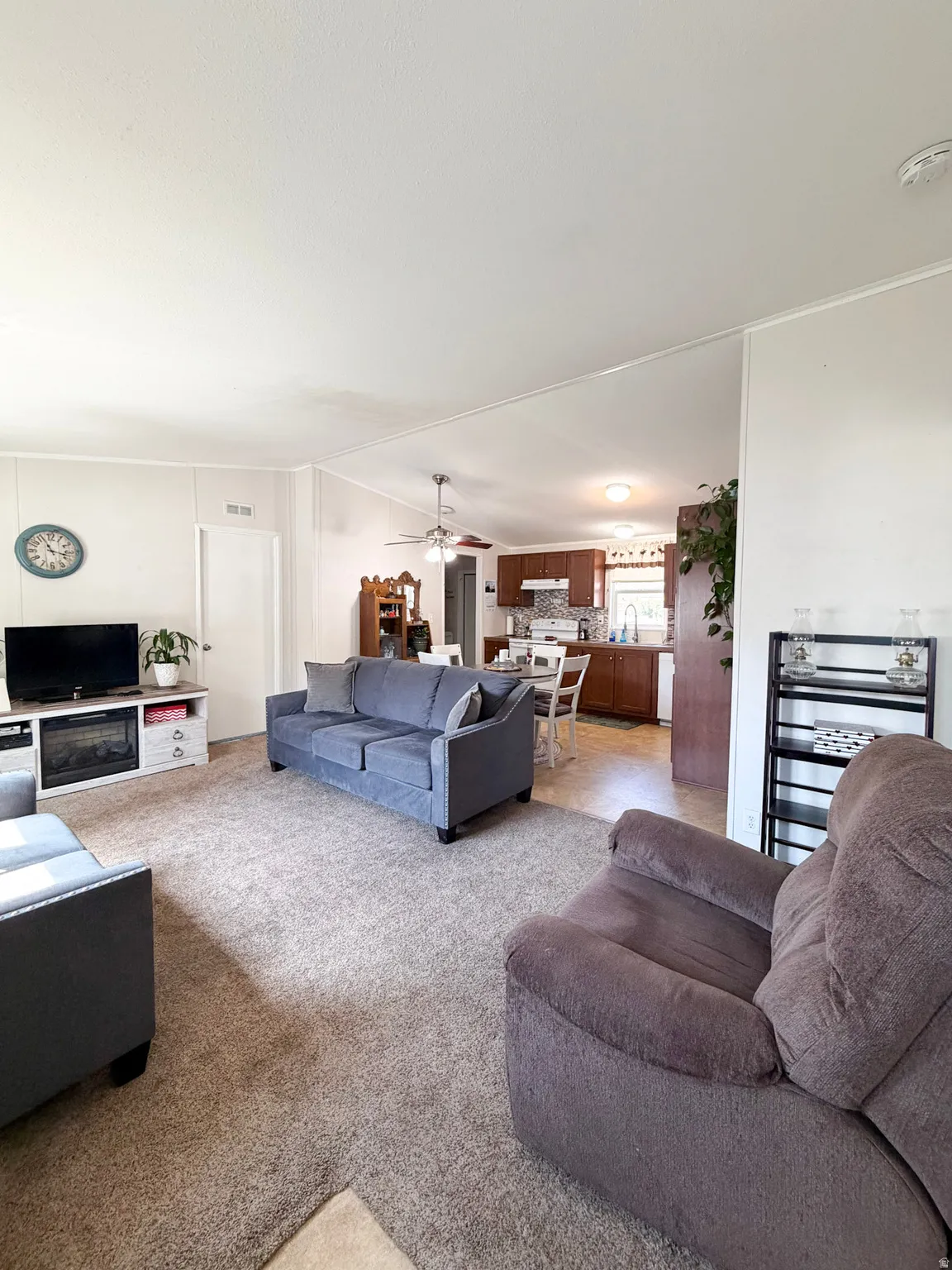 Open-concept living space featuring neutral-toned carpeting, a built-in electric fireplace, and a ceiling fan