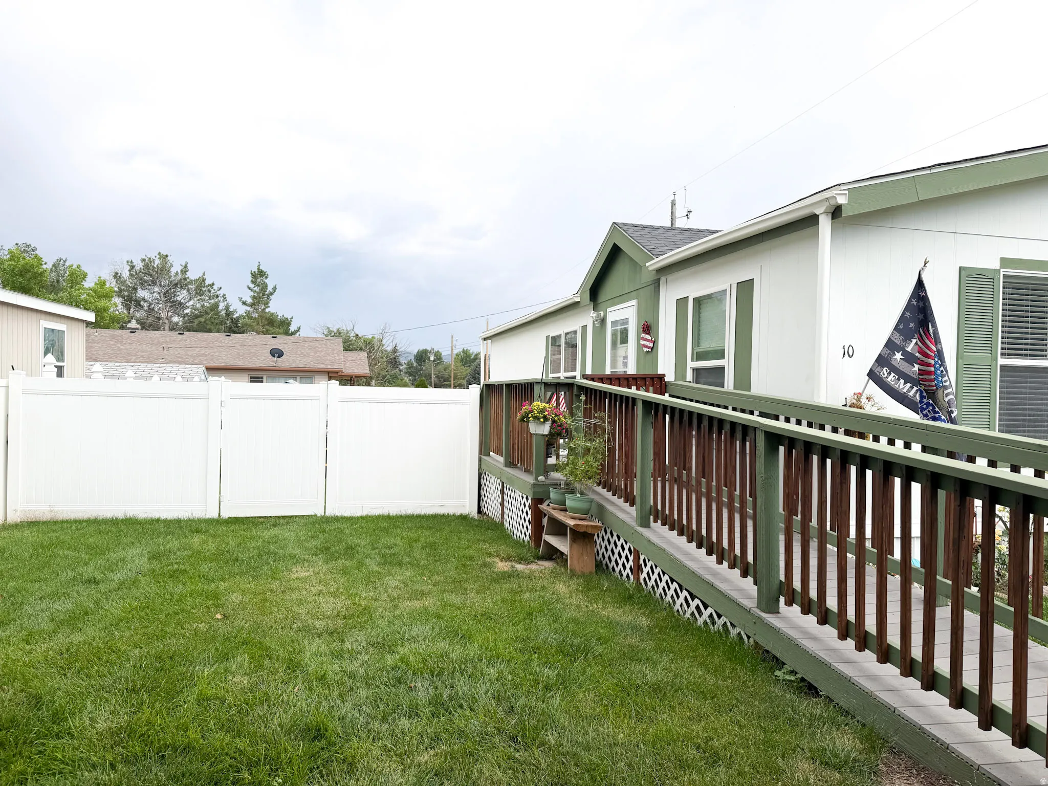 Exterior featuring white siding with green trim, a covered porch, a ramp entry, green window shutters, and a white privacy fence enclosing a lawn area