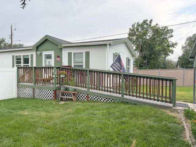 Exterior featuring a white facade with green trim, a covered porch entry, a wooden deck, an integrated access ramp, and a white lattice skirt