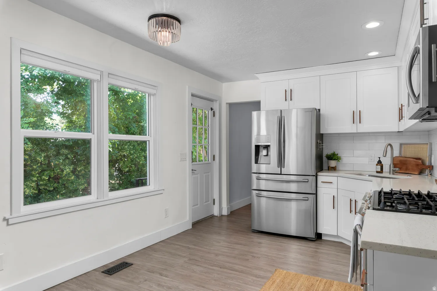 Kitchen featuring white shaker cabinetry, stainless steel appliances, light wood-finish flooring, and subway tile backsplash