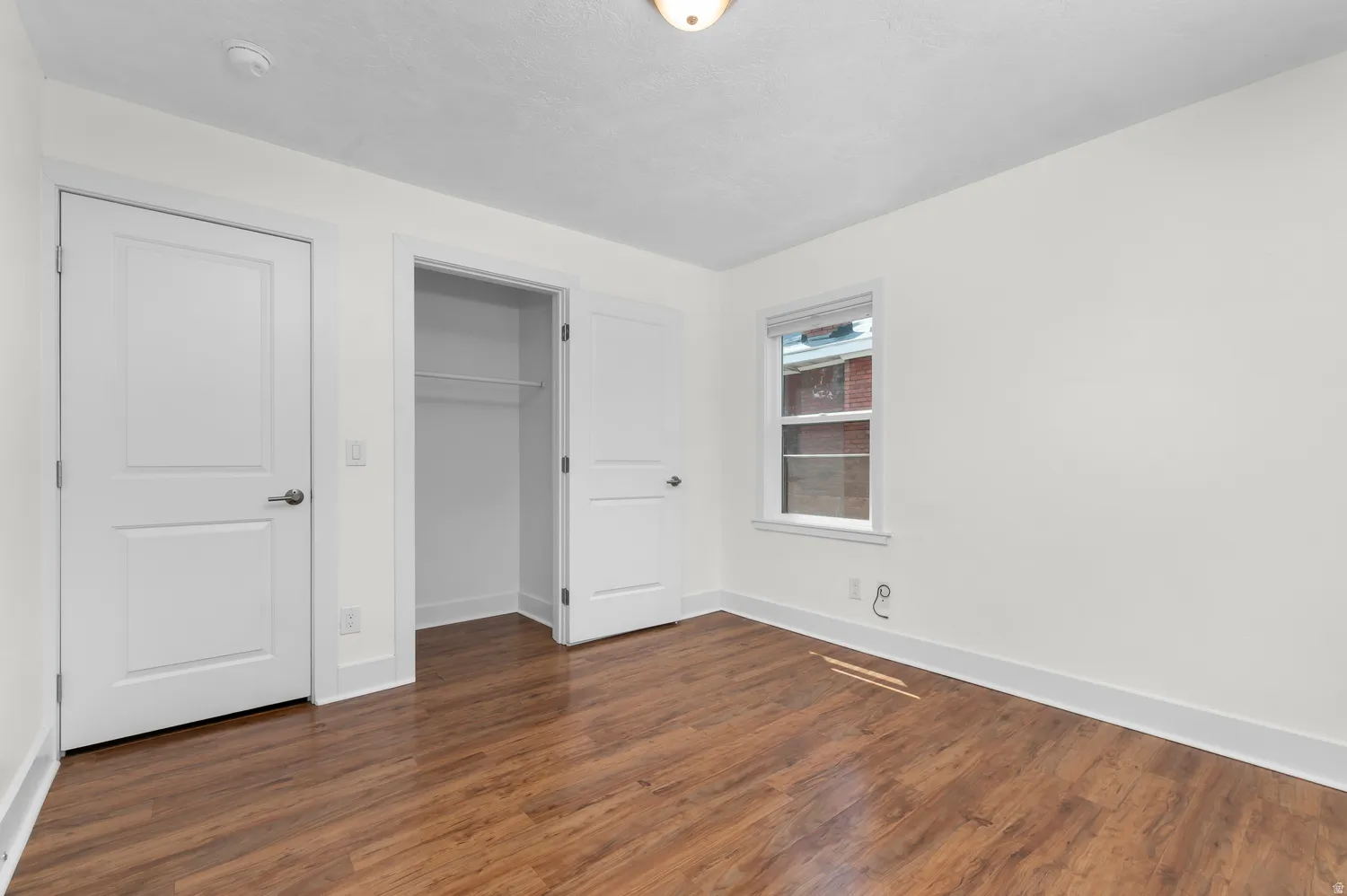 Interior room featuring wood-finish flooring, white walls, and a single window with white trim