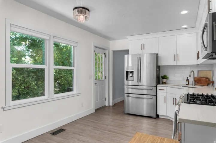 Kitchen featuring white shaker cabinetry, stainless steel appliances, light wood-finish flooring, and subway tile backsplash