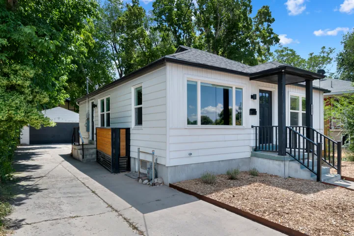 White siding exterior with a dark-trimmed covered porch, black entry door, and large picture windows