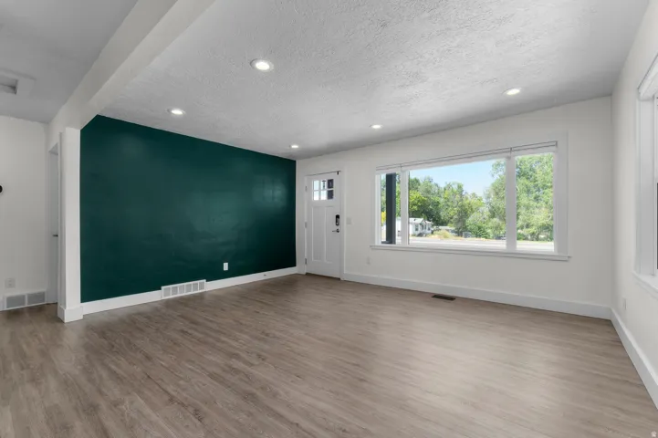 Spacious interior featuring a large picture window, wood-finish flooring, recessed lighting, a contrasting accent wall, and a craftsman-style entry door
