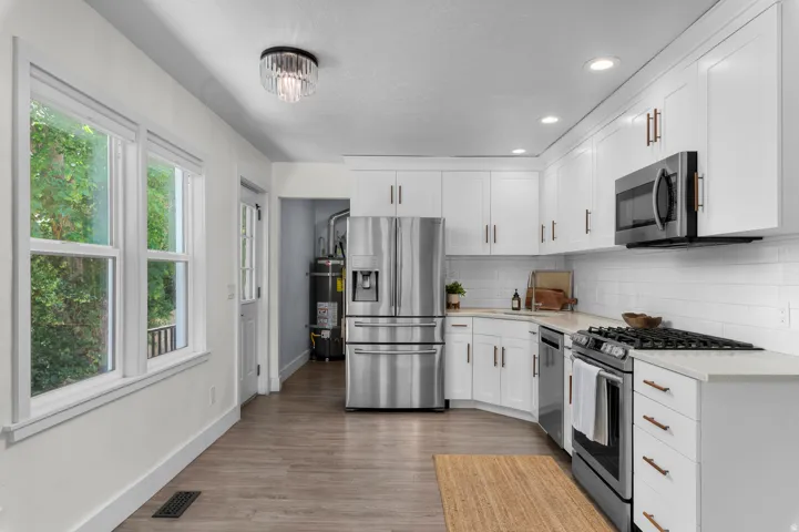 Modern kitchen featuring white shaker cabinetry, stainless steel appliances, light-toned countertops, subway tile backsplash, and wood-finish flooring