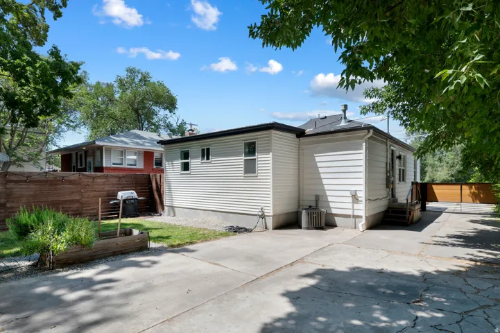 Rear exterior featuring white horizontal siding, a concrete driveway, a wooden privacy fence, a small grassy area, and mature perimeter trees