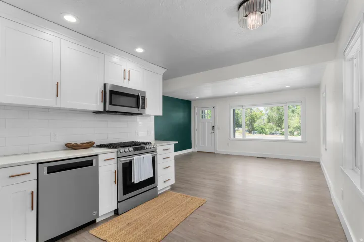 Kitchen featuring white shaker cabinetry, stainless steel appliances, white subway tile backsplash, and light-toned countertops