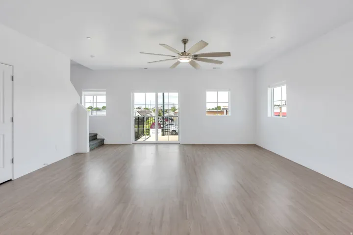 Spacious room featuring wood-finish flooring, white walls, and a multi-blade ceiling fan with integrated lighting