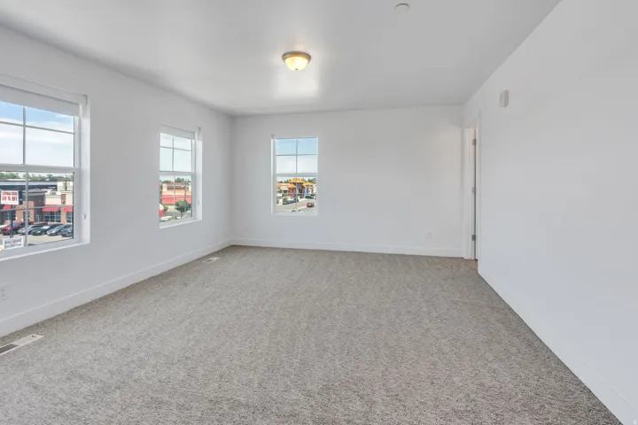 Bright interior space featuring a textured gray carpet, three large windows with white trim, and a ceiling-mounted light fixture