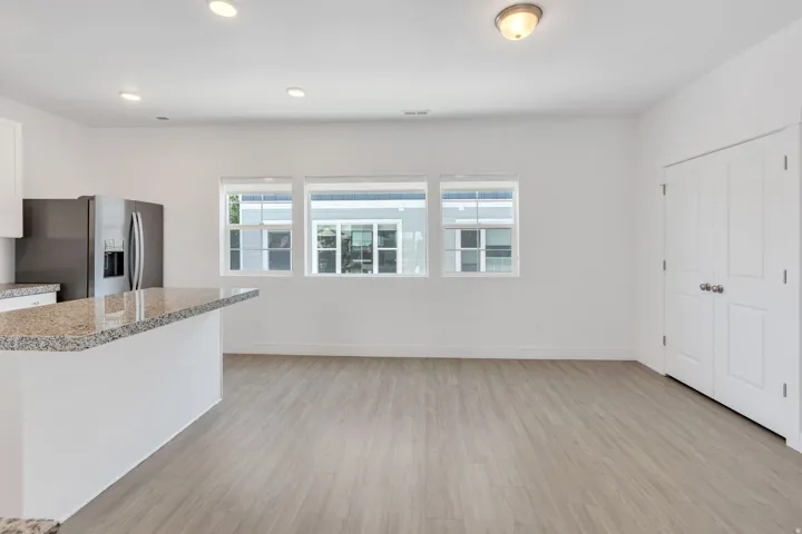 Kitchen island with a granite countertop, stainless steel refrigerator, recessed lighting, wood-finish flooring, and a bank of three windows