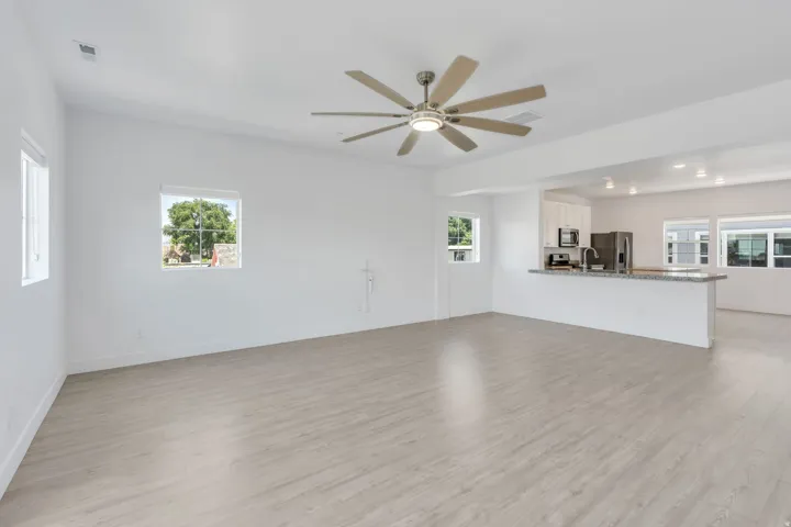 Open-concept living area featuring light wood-finish flooring, a contemporary ceiling fan, and multiple windows