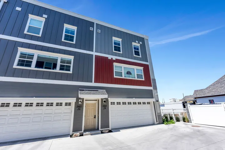 Three-story residential building featuring vertical panel siding in dark gray, light gray, and red accents