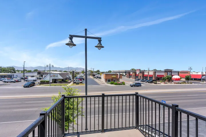 Balcony with black metal railings overlooking a commercial thoroughfare and distant mountains under a clear sky