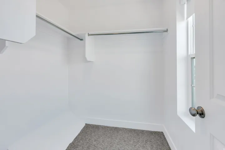 Walk-in closet featuring white walls, grey carpet flooring, multiple hanging rods, and a window for natural illumination