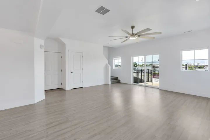 Open-concept living area featuring light wood-finish flooring, white walls, and a contemporary ceiling fan