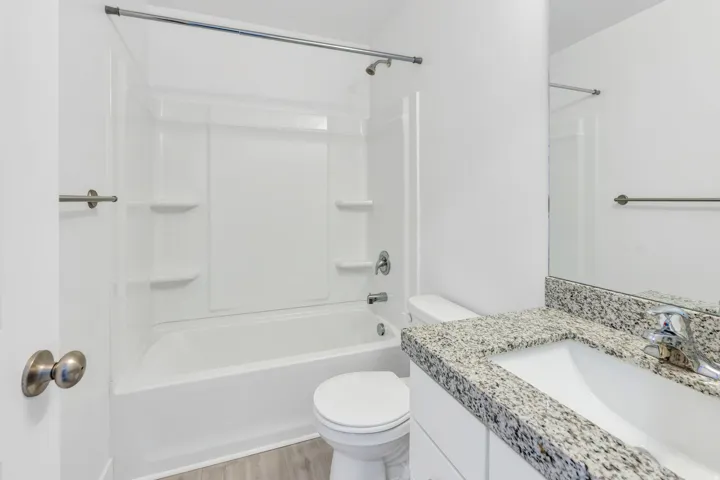 Bathroom with a white tub-shower combination, a vanity featuring a granite-style countertop, an undermount sink, and wood-finish flooring