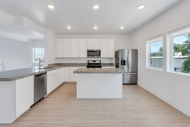 Contemporary kitchen featuring white cabinetry, stone countertops, stainless steel appliances, a central island, and wood-finish flooring