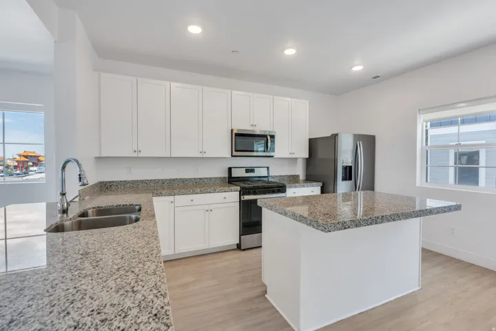 Modern kitchen featuring light wood-finish flooring, white cabinetry, granite countertops, and stainless steel appliances