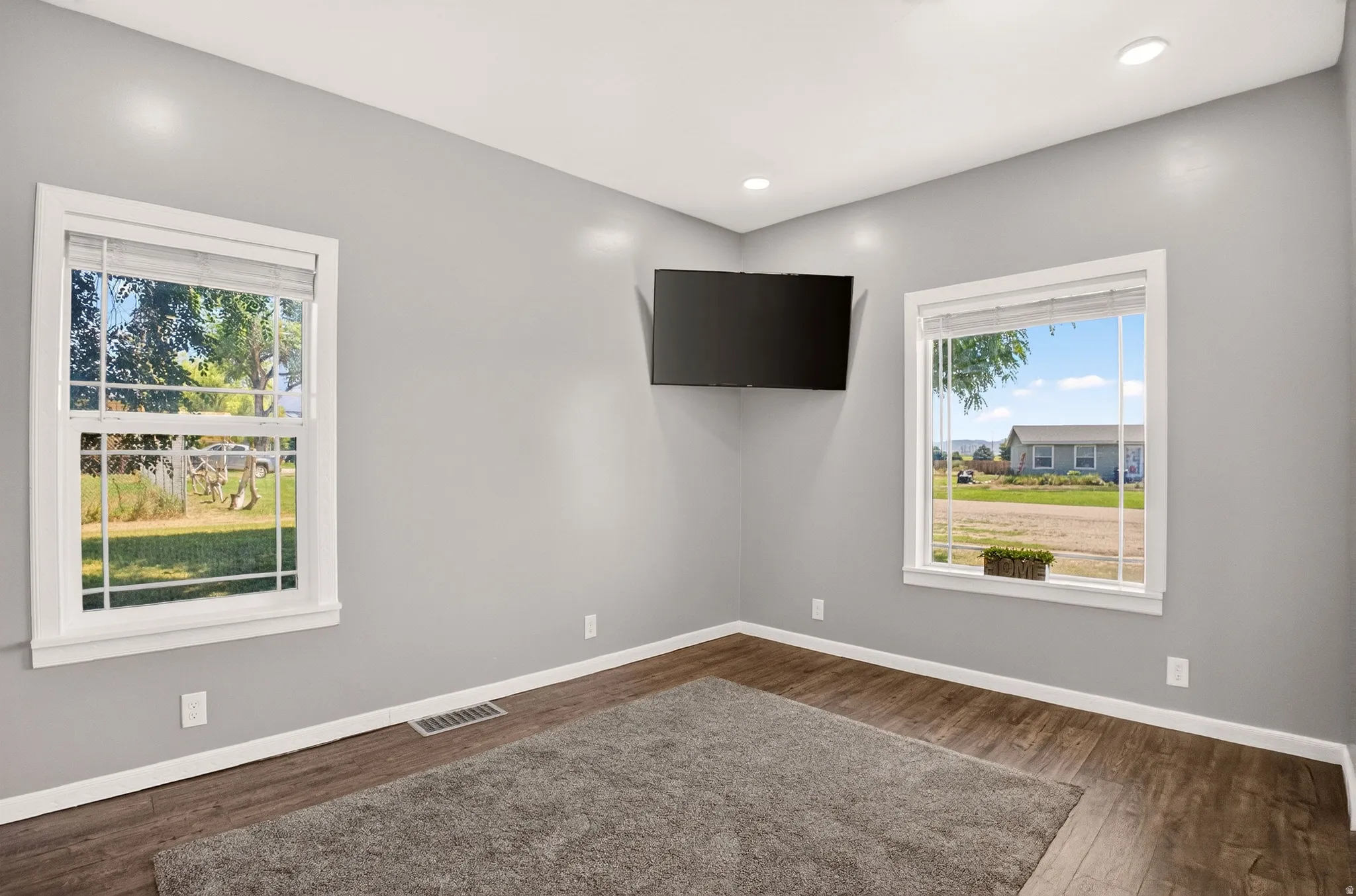 Bright interior space with two large windows, wood-finish flooring, white baseboards, and recessed ceiling lighting